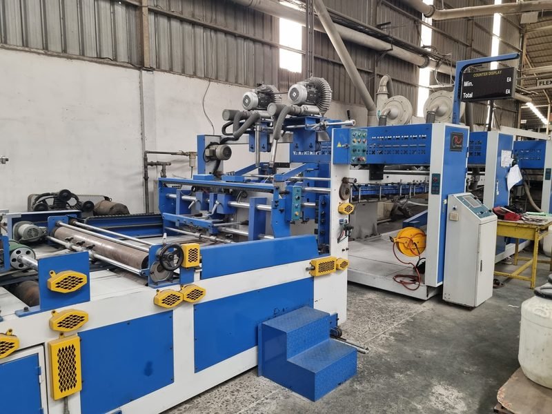 Mesin produksi karton box berwarna biru dan putih di fasilitas Multi Artha Abadi
